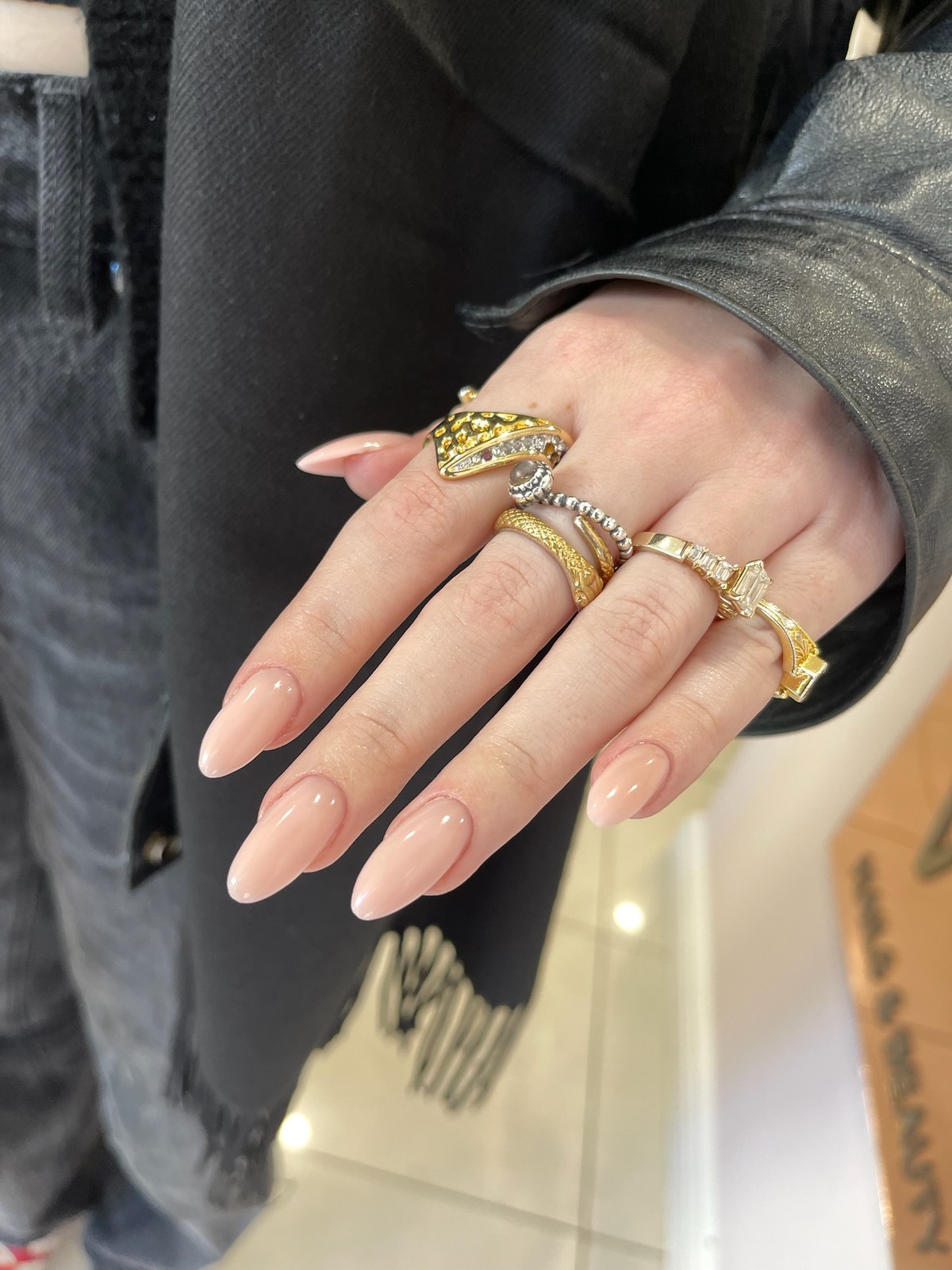 Nude glossy almond manicure with layered gold rings
